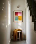 Abstract color block art painting on a wall above a stool with a yellow blanket in a room.