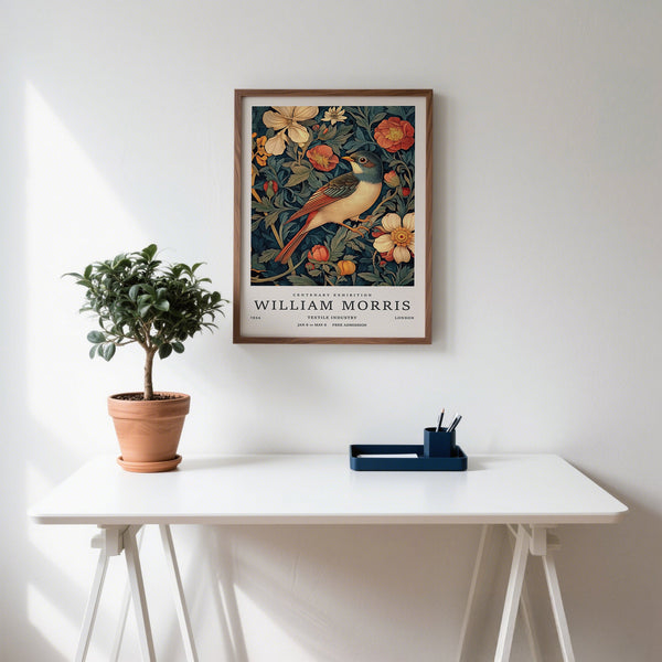 Framed artwork of a bird and flowers on a wall above a white desk with a plant and small tray.