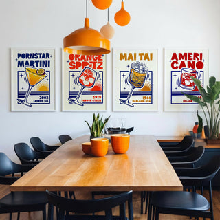A dining room scene with a wooden table, black chairs, orange pendant lights, and four framed retro-style posters on the wall. The posters feature bold text including 'PORNSTAR MARTINI', 'ORANGE SPRITZ', 'MAI TAI', and 'AMERI CANO' with illustrated drink glasses and starburst graphics.