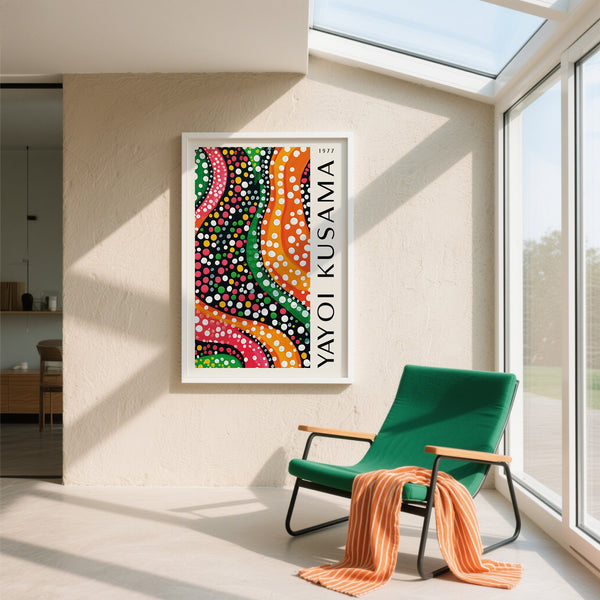 Colorful abstract artwork by Yayoi Kusama on a wall in a modern room with a green chair and orange blanket.