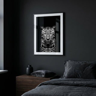 Framed artwork of a leopard on a dark wall above a bed.