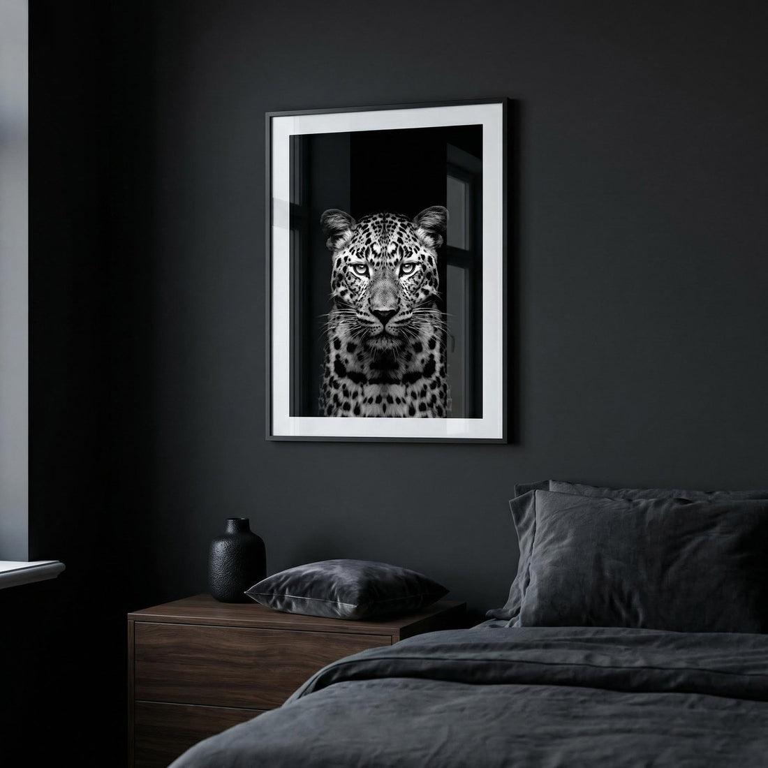 Moody bedroom with black walls, charcoal bedding, a walnut bedside table and a black and white leopard print in a white mount