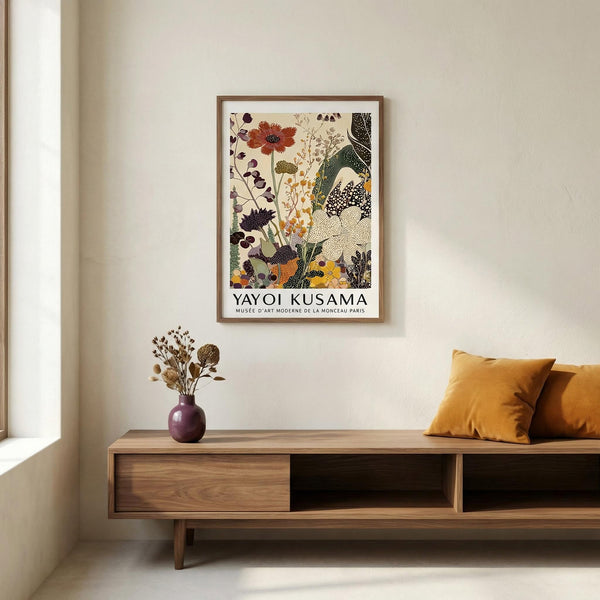 Framed Yayoi Kusama artwork on a wall above a wooden console table with a vase and pillows.