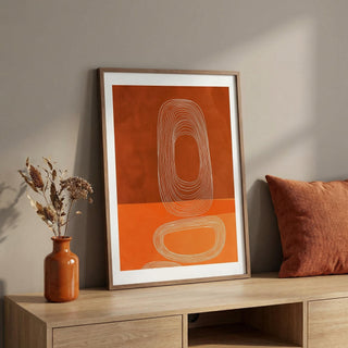 Framed abstract artwork with orange background and brown frame on a wooden shelf.