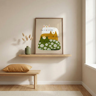 Framed artwork of a cat and flowers on a wall above a wooden shelf with a vase and pillow.