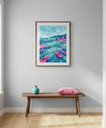 Framed artwork of a colorful coastal scene on a wall above a wooden bench with a vase and pillow.