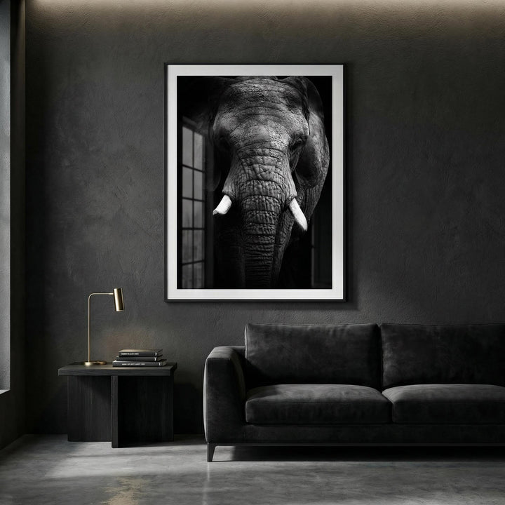 Elephant print framed on a dark wall above a black sofa with a side table and lamp