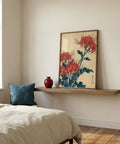 Framed artwork of red flowers on a wall above a bed with a blue pillow.