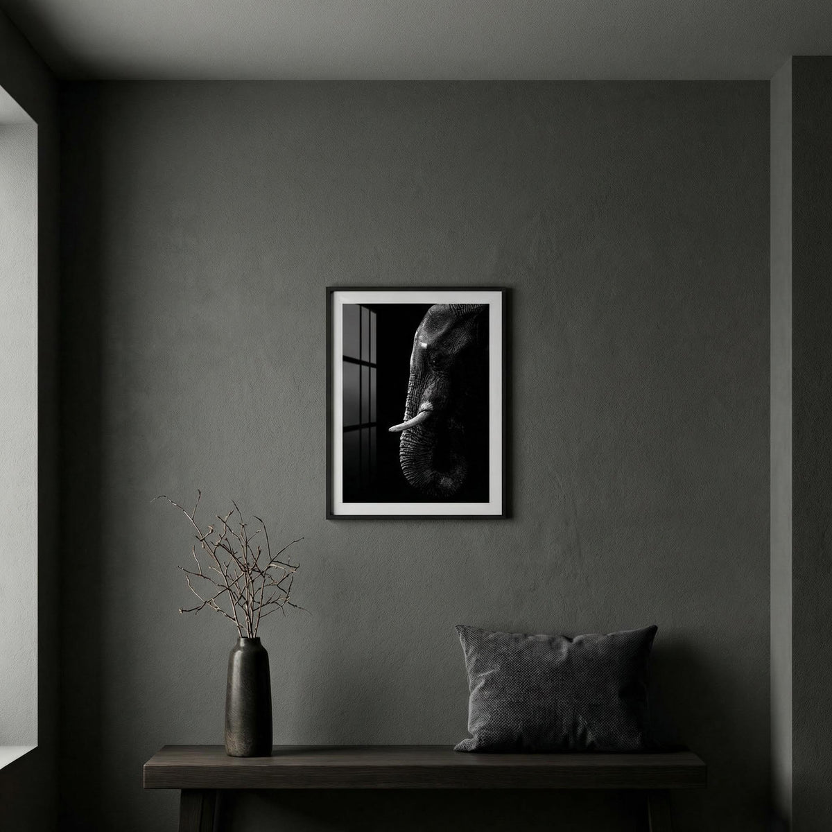 Framed black and white artwork of an elephant on a gray wall above a wooden table with a vase and pillow.