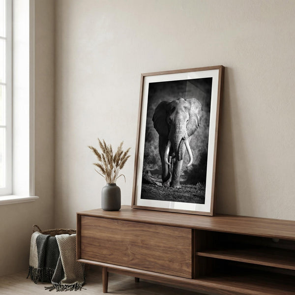 Framed black and white elephant print on a wooden sideboard in a room with natural light.