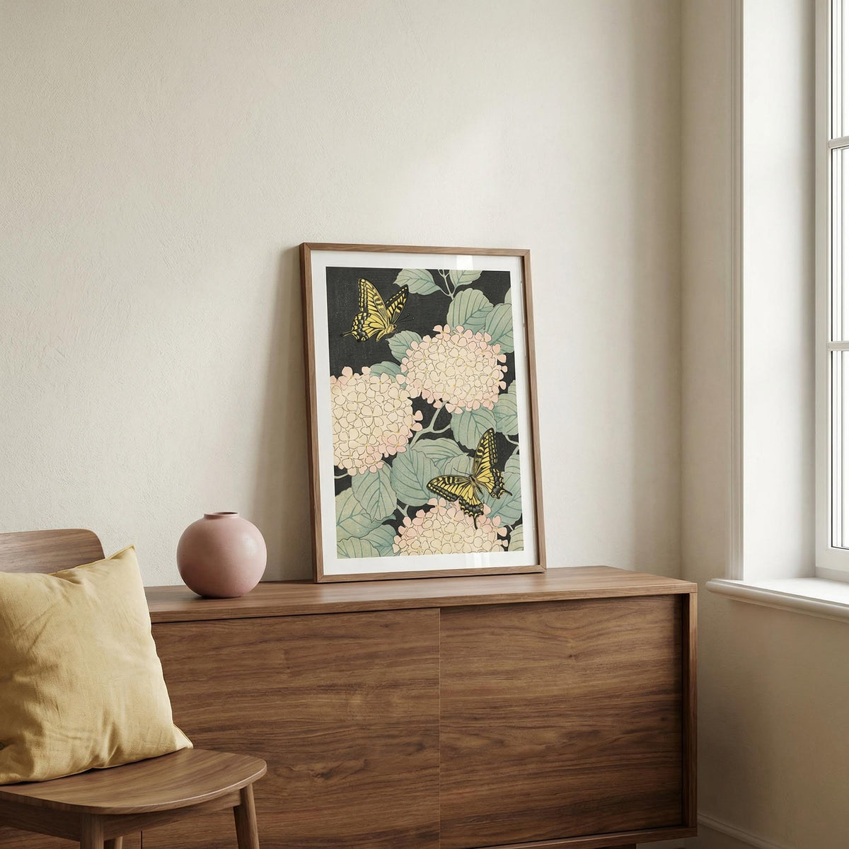 Framed floral and butterfly artwork on a wooden dresser with a window in the background.