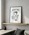 Framed artwork of a dog with sunglasses and 'FETCH THIS' text on a wall above a desk.