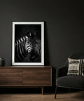 Framed zebra print on a dark wall above a wooden cabinet with a black armchair.