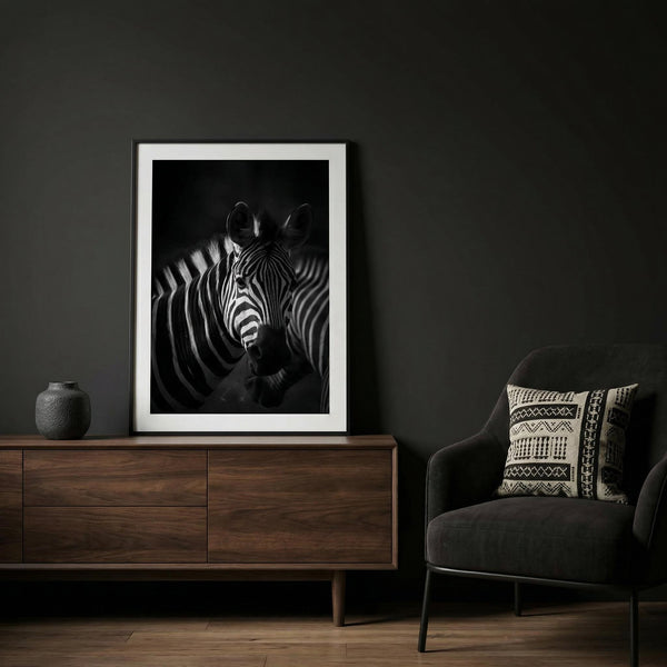 Framed zebra print on a dark wall above a wooden cabinet with a black armchair.