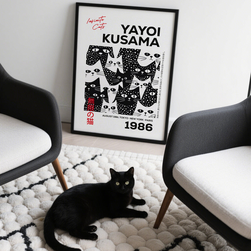 Black cat lying on a white rug with a framed Yayoi Kusama poster in the background.