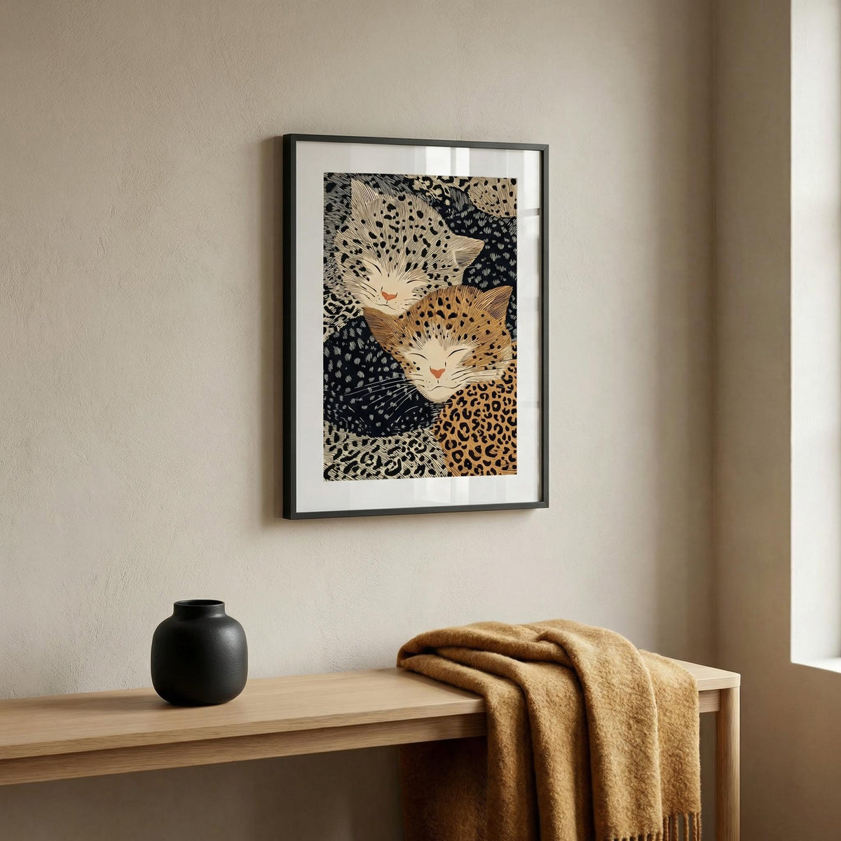 Framed artwork of two stylized leopards on a beige wall above a wooden console table with a vase and blanket.
