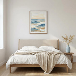 Beige bed with white bedding and a beige blanket in a room with a painting on the wall.