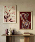 Two framed artworks on a wall above a wooden console table with decorative vases and books.