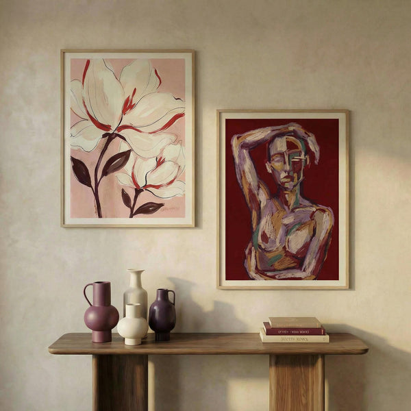 Two framed artworks on a wall above a wooden console table with decorative vases and books.