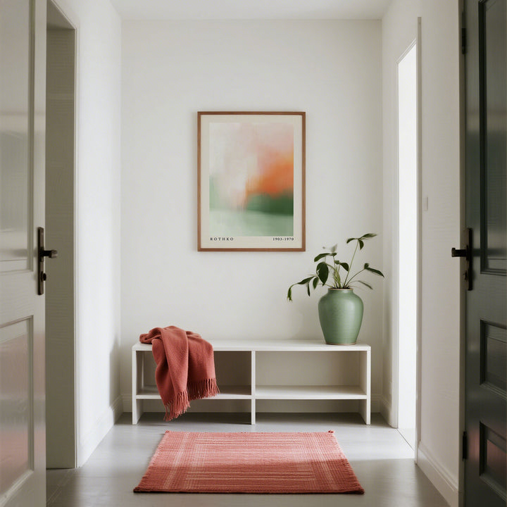 Calming wall art with abstract peach and green fields above a sideboard and plant in a white hallway