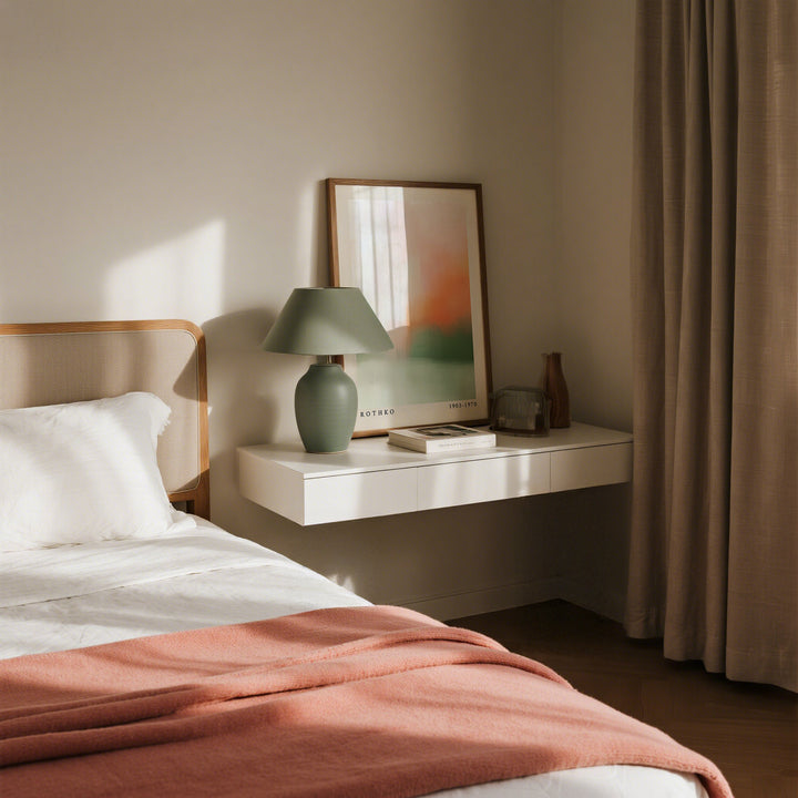 Calming wall art with abstract peach colour fields leaning on a floating shelf beside a green lamp in a bedroom