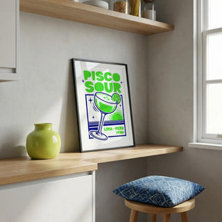 Framed 'Pisco Sour' poster on a shelf with a green vase and blue cushion.