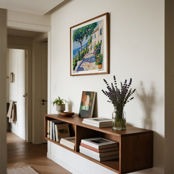 Wooden shelf with books and a vase of flowers, framed prints of Amalfi above on a white wall.