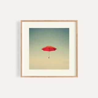Framed print of a red umbrella floating in a minimalist cloudy sky with pale colours