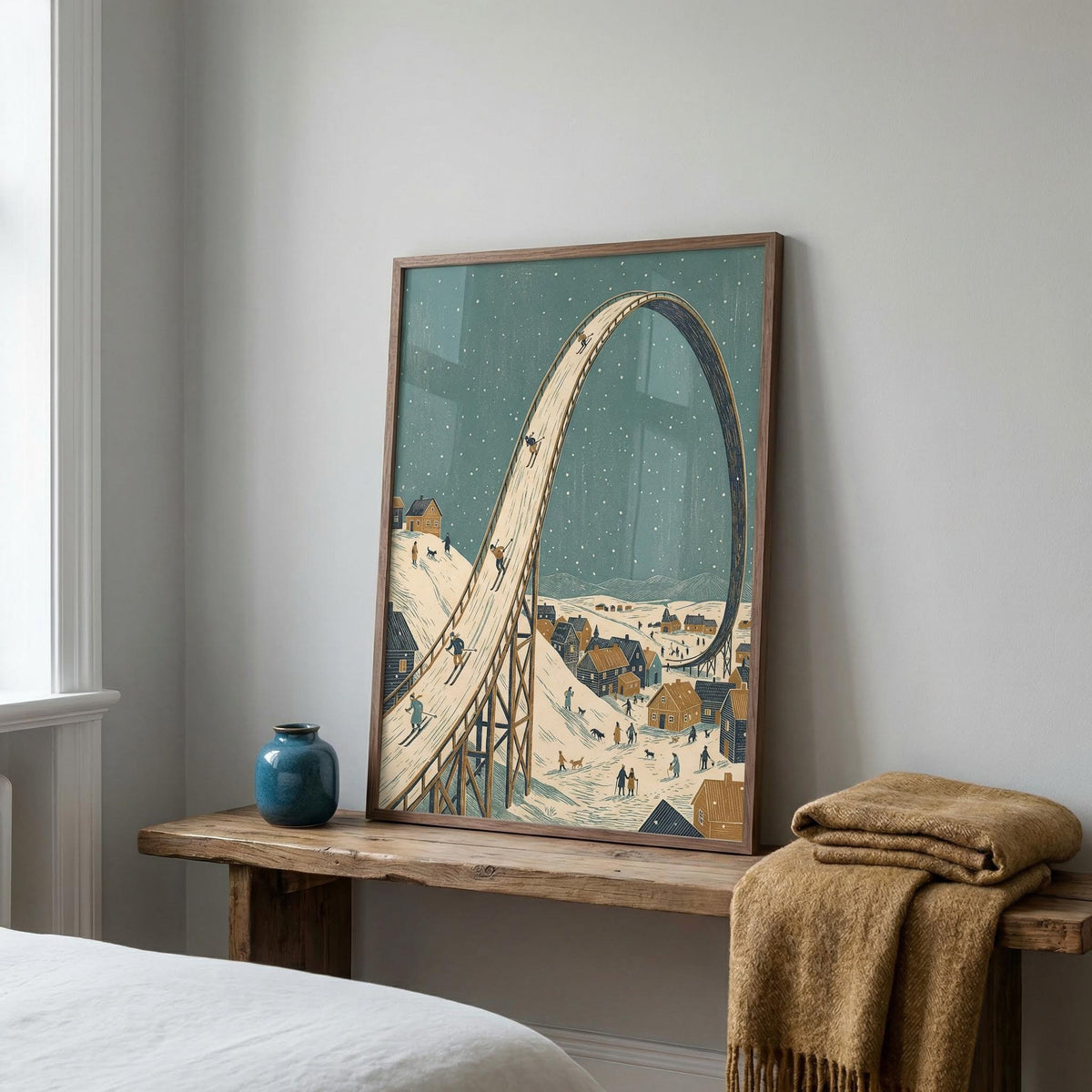 Framed artwork of a ski scope scene on a wall above a wooden bench with a vase and blanket.
