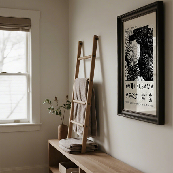 Room interior with a wooden ladder, folded towels, and a framed Yayoi Kusama black and white artwork on the wall.