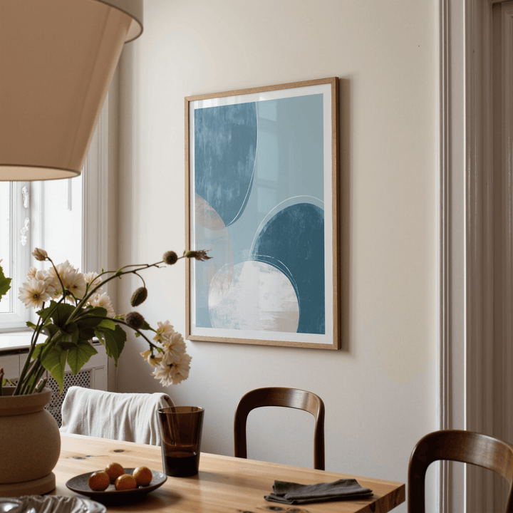 Abstract Blue Art Print on a beige wall with blue and white circles above a wooden dining table with flowers