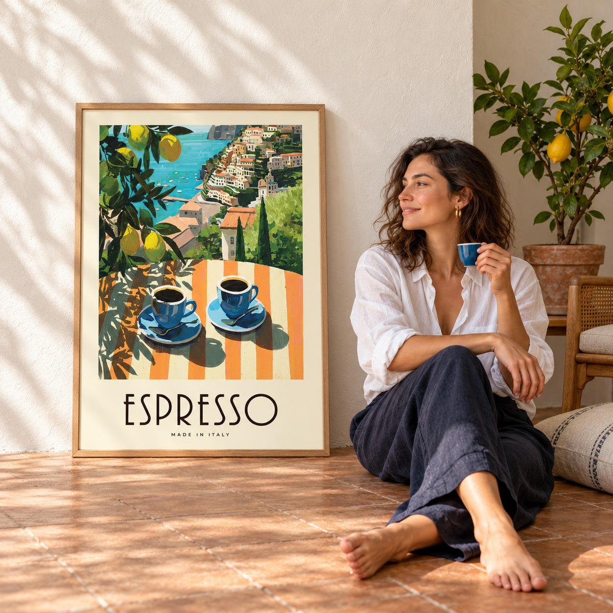 Woman with an espresso sitting beside the Amalfi Espresso print leaning on a sunny wall