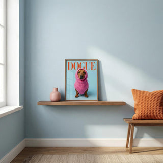 Framed artwork of a dog wearing a pink sweater on a shelf against a light blue wall.