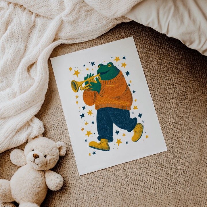Frog Playing Trumpet Art print flat on a carpet next to a teddy bear and a cream knitted blanket