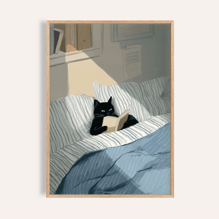 Framed Cat Reading Book wall art of a black cat with a beige book on striped bedding in soft lighting