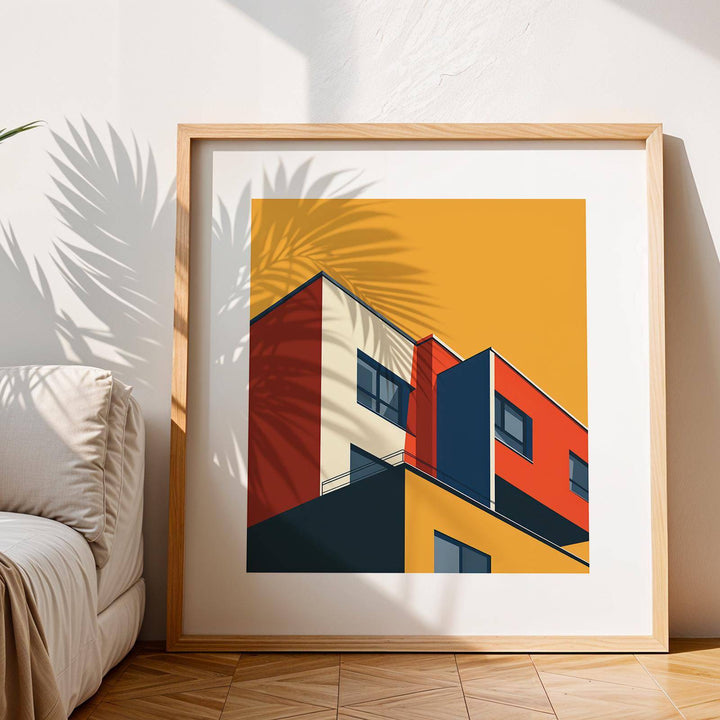 Framed Bauhaus Architecture Print of a minimalist modern building with red and yellow colours leaning on a wooden floor sofa nearby