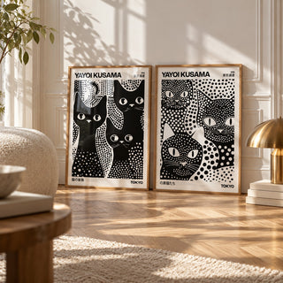 Black and White Cat Prints Set of 2 styled leaning on a herringbone floor between a boucle cushion and a brass mushroom lamp: 3 Black Cats and Kusama Black Cats shown framed side by side (frames not included)