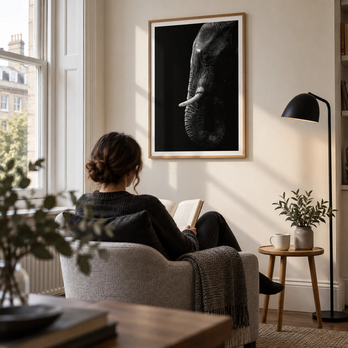 Black Elephant Wall Art, framed on the wall of a calm reading corner beside a tall sash window in a UK flat with a warm white wall in a living room