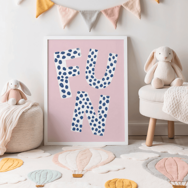 Fun typography wall art with blue polka dotted letters on pink background leaning on floor in a child's room with plush toys