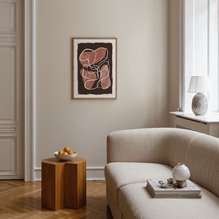 Abstract earth tone print with brown and terracotta shapes hanging above a wooden side table with a bowl of fruit