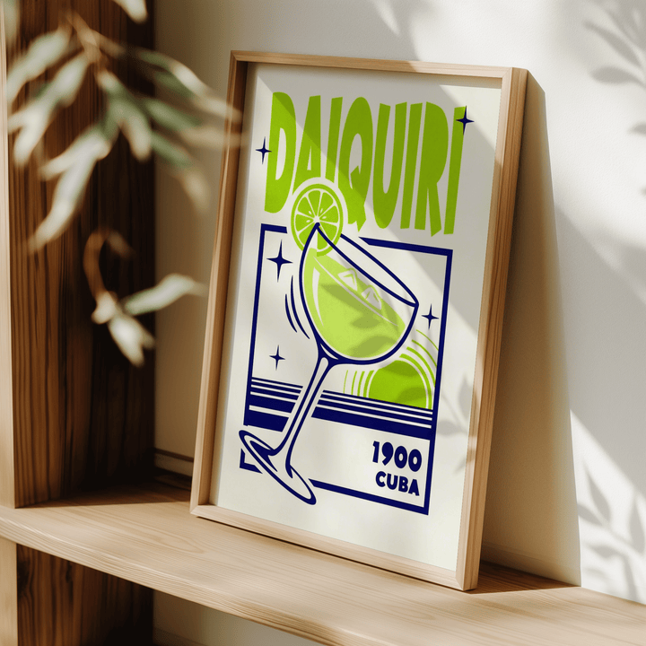 Framed Daiquiri art print with green and navy minimalist style leaning on a shelf near plant shadows