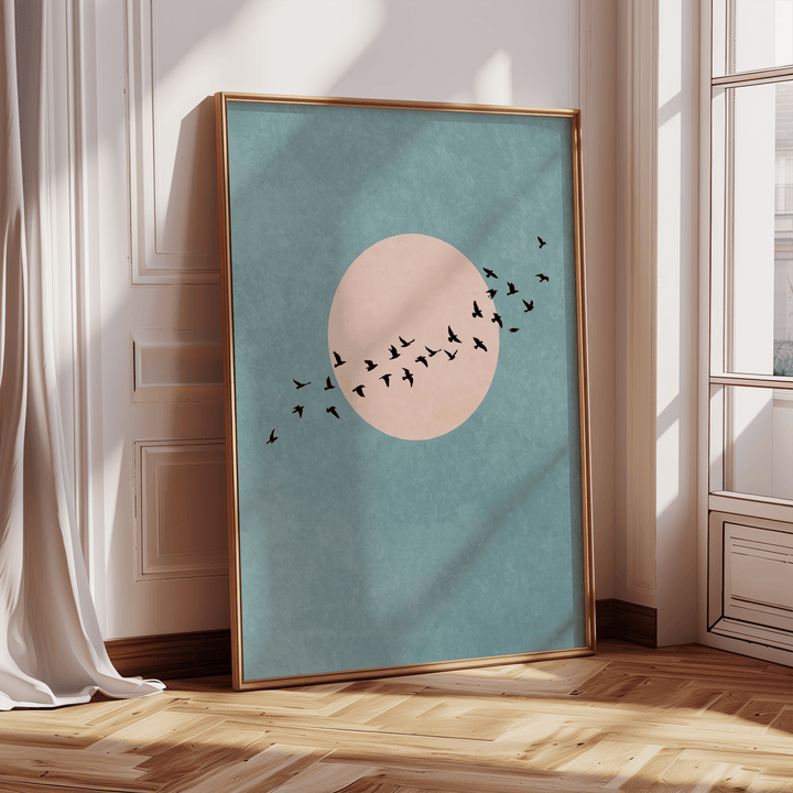 Print leaning on a floor showing a flock of birds in flight against a pink circle on a blue background in natural light