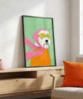 Framed artwork of a dog wearing sunglasses and a pink hood on a wooden cabinet with an orange pillow.