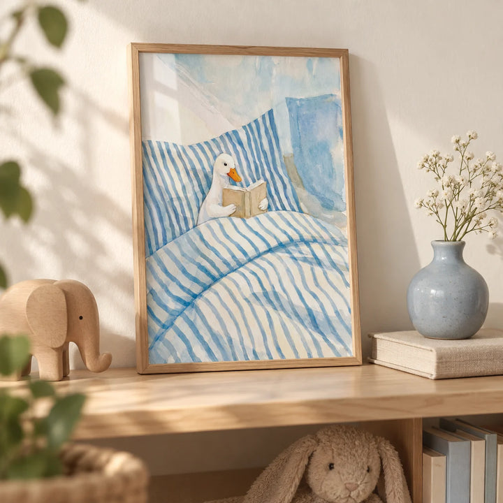 Duck Reading Art Print, a small A4 framed print leaning on a pale oak nursery shelf
