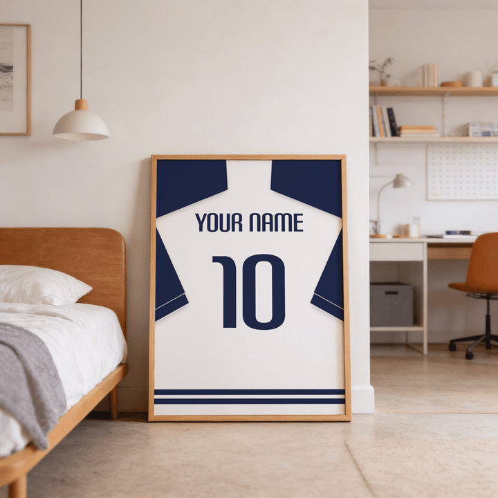 Print leaning on the floor of a bedroom showing a minimalist football shirt poster in white with navy sleeves and navy number