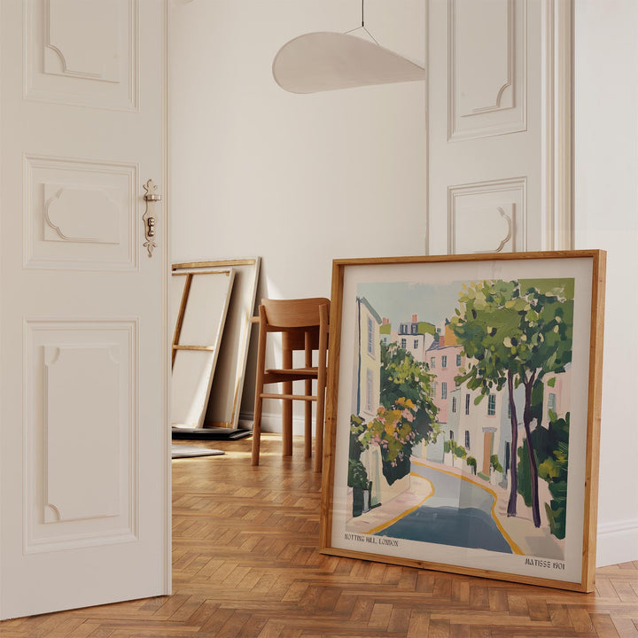 Print leaning on a parquet floor showing a pastel coloured Notting Hill street illustration with trees and buildings