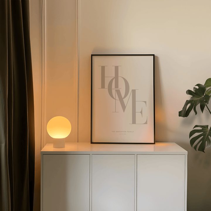 Framed Home Beige Personal Print leaning on a white cabinet with lamp and plant nearby