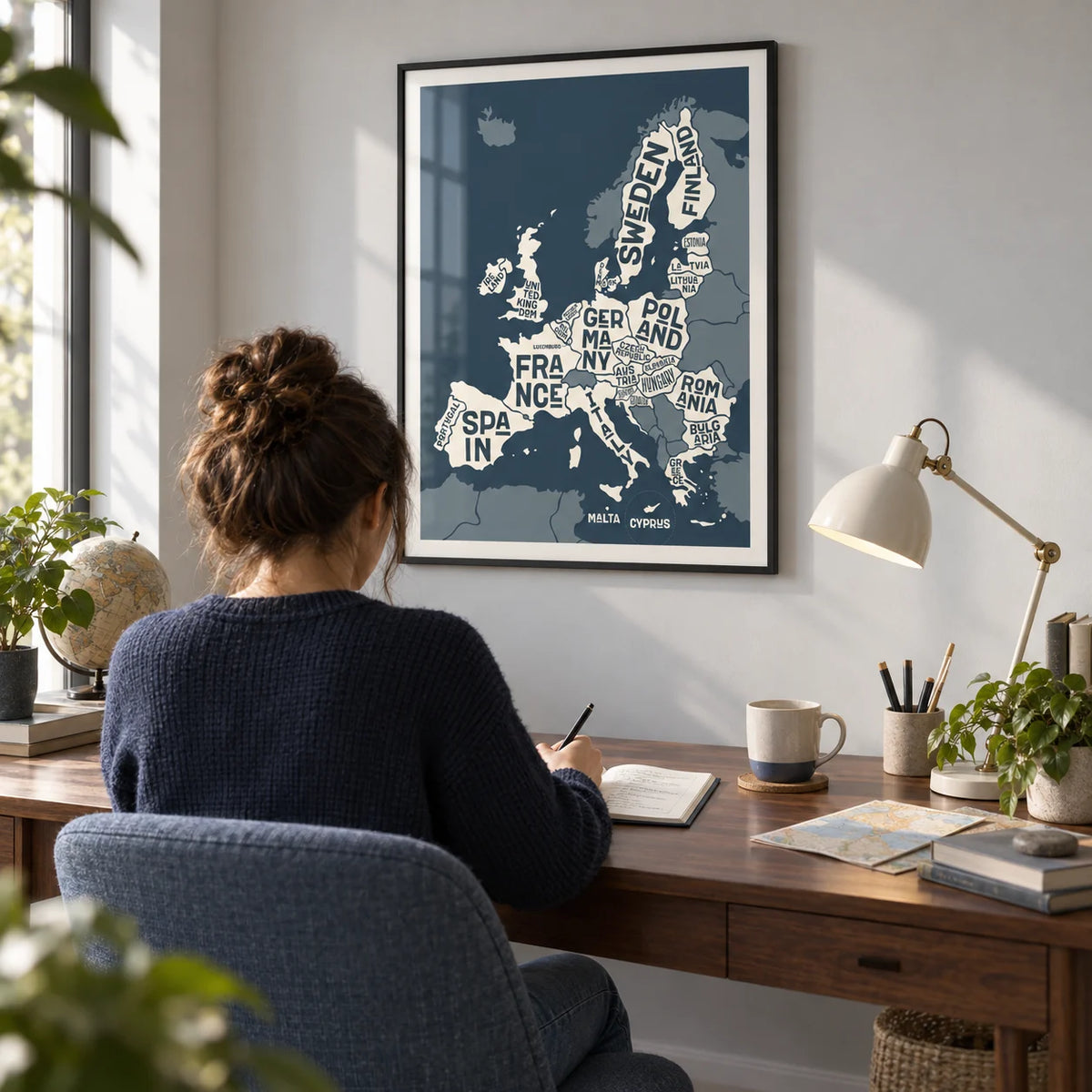 Europe Map Print, framed on the wall of a travel lover's compact home study with a pale grey wall and a walnut desk