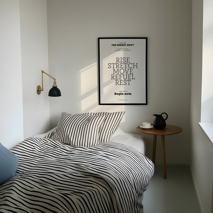 Posters with Inspirational Sayings framed print with motivational text in black and white above a bed with striped bedding and a wall lamp