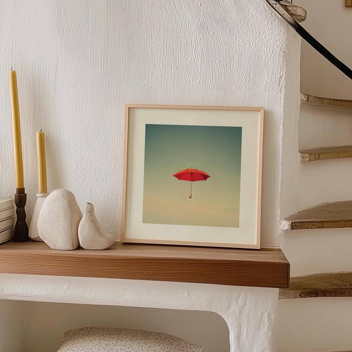 Framed Surreal Wall Art of a red umbrella floating against blue sky on a wooden shelf with candles